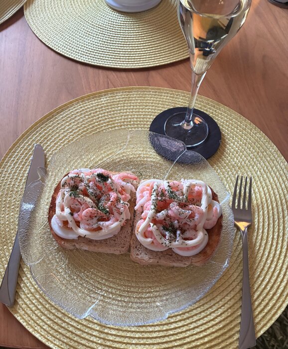 Räkmackor på en tallrik med glas champagne bredvid, placerat på ett gult underlägg.