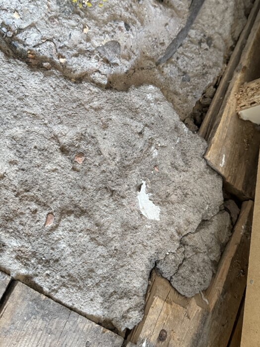 Golvbrädor med trasigt hörn, synliga lager av sand/lera och en svart kabel under, omgivna av gammalt trägolv i ett äldre hus.