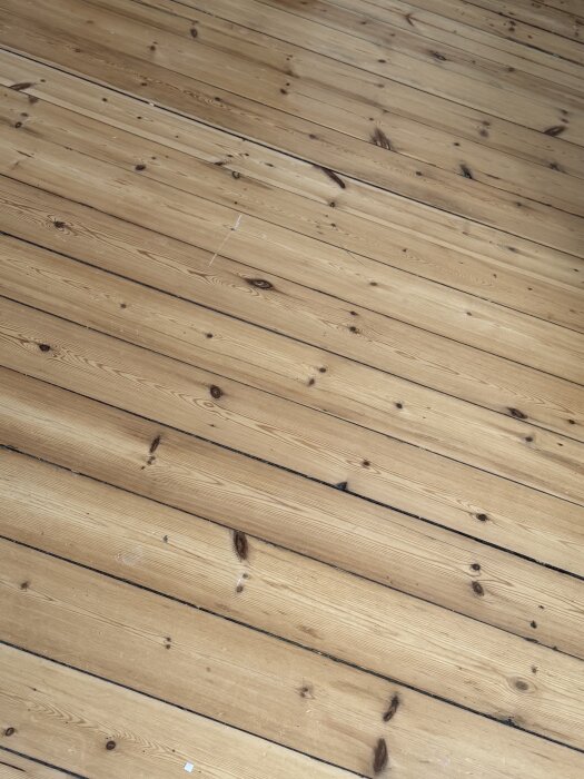 Trägolv i ett äldre hus, med synliga brädor och en del små skavanker. Golvets utseende diskuteras i ett inlägg om renovering.