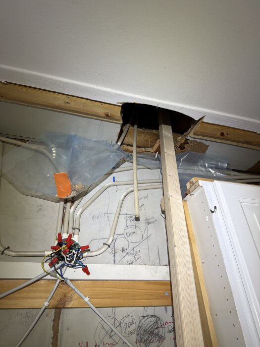 Tak med hål och blottlagda kablar, träsupport och plast, ritningar på väggen. Renovationskaos i rummet.