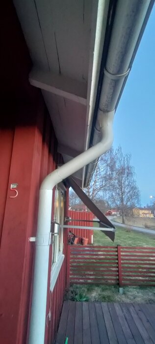 Stuprör vid röd husfasad, med vit hängränna som påverkar planerat plasttak på altan.