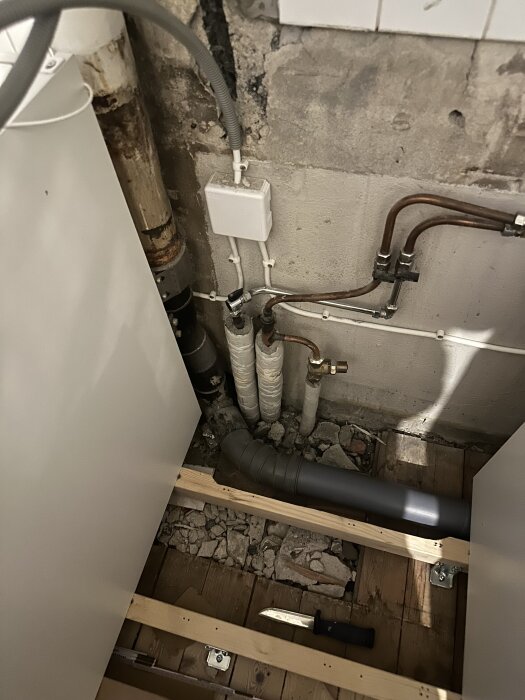 Rör och avloppskopplingar i en vägg med synliga träbalkar och en kniv på golvet vid renovering av ett 40-talskök.