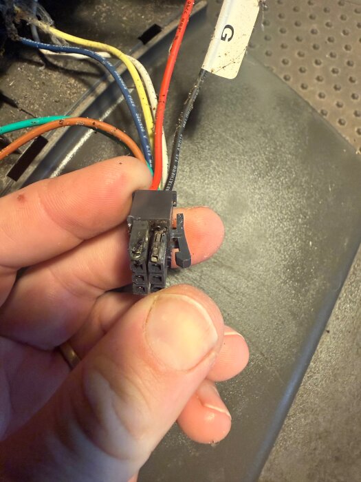 Närbild av en hand som håller i ett elektriskt kopplingskort med flera färgade kablar.