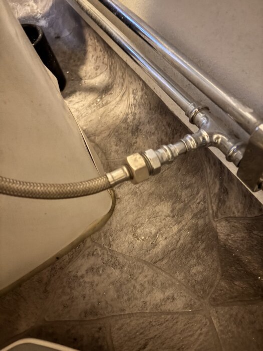 Vattenrör och kopplingar under badrumstoalett där en slang är ansluten till en t-koppling, del av inlägg om tvättmaskinsinstallation.