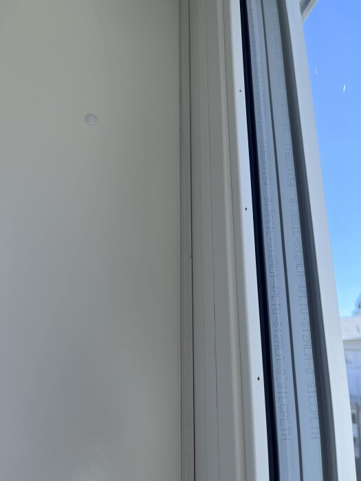Fönster inifrån sett, delvis stängt och oöppningsbart, med utsikt mot klarblå himmel.