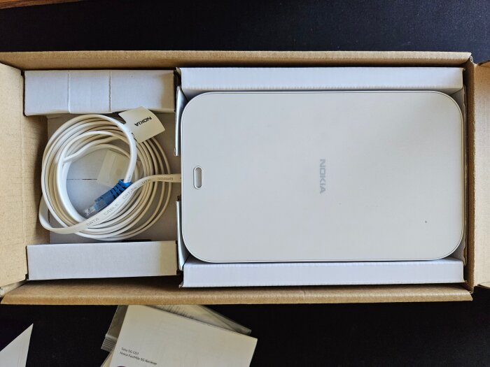 Kartong med en vit Nokia 5G-mottagare och medföljande vit datakabel, liggande på ett bord.