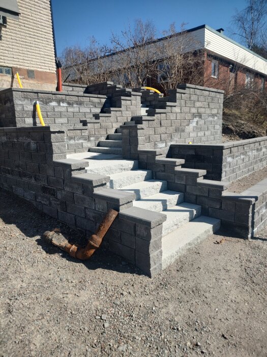 Nybyggd mur och trappa av gråa betongblock från Benders, med synliga skåror och färgvariation i torrt och fuktigt tillstånd.
