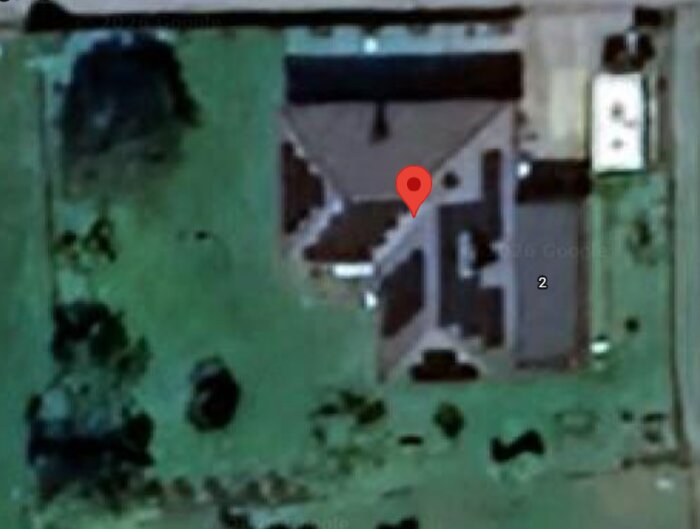 Flygfoto över tomt med gräsmatta och hus. En röd markör visar en specifik plats, omgiven av gröna ytor.