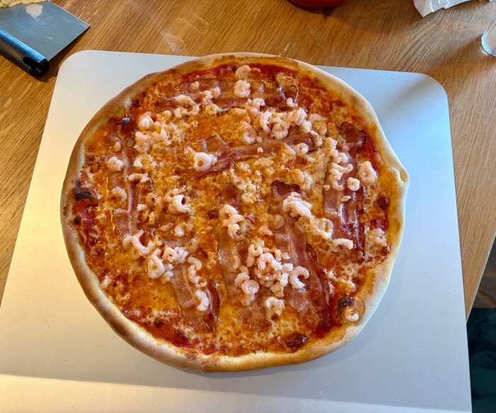Hemlagad pizza med räkor och bacon på en skärbräda.