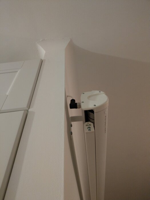 Euroscreen Diplomat projektorduk monterad på vägg vid taket, del av installation synlig med vita paneler och fäste.
