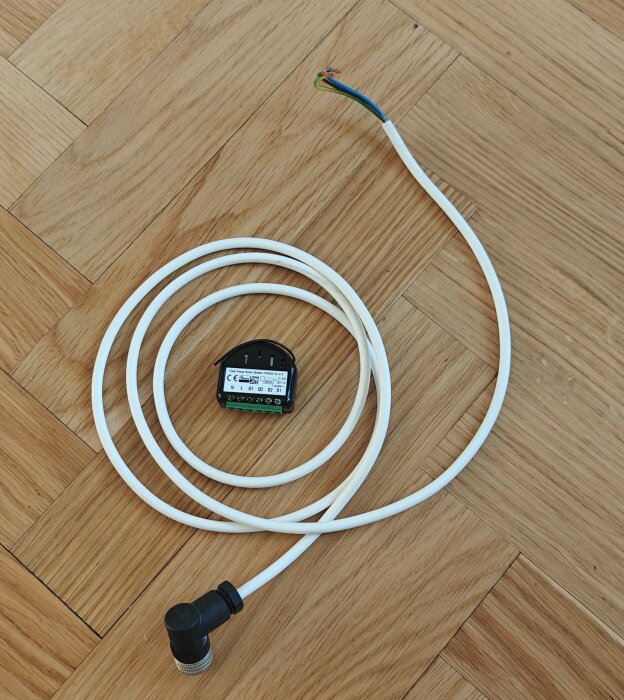 Kabel och z-wave puck för Euroscreen Diplomat Tab Tension React 3.0 ligger på ett trägolv.