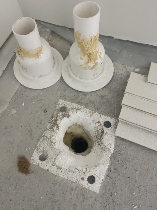 Golvbrunn öppning med frigolit, två PVC-rör insatta med skum, omgivna av betong, byggprojekt för anslutning och fixering av golvbrunn.