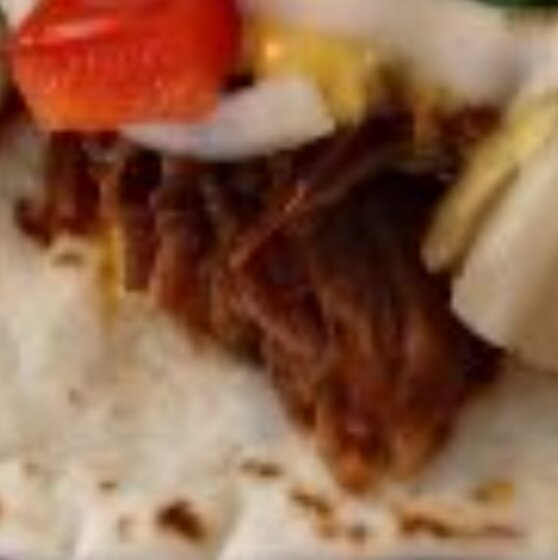 Taco med kött, lök, tomat och sås på ett tortillabröd.
