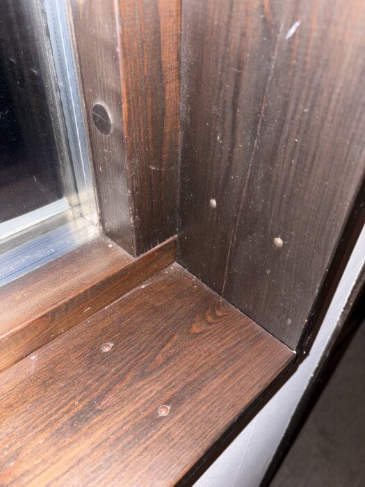 Mörka fönstersmygar vid ett glasfönster, fästa med spikar. Från 70-80-talet, önskan att byta till ljusare eller trärena smygar.