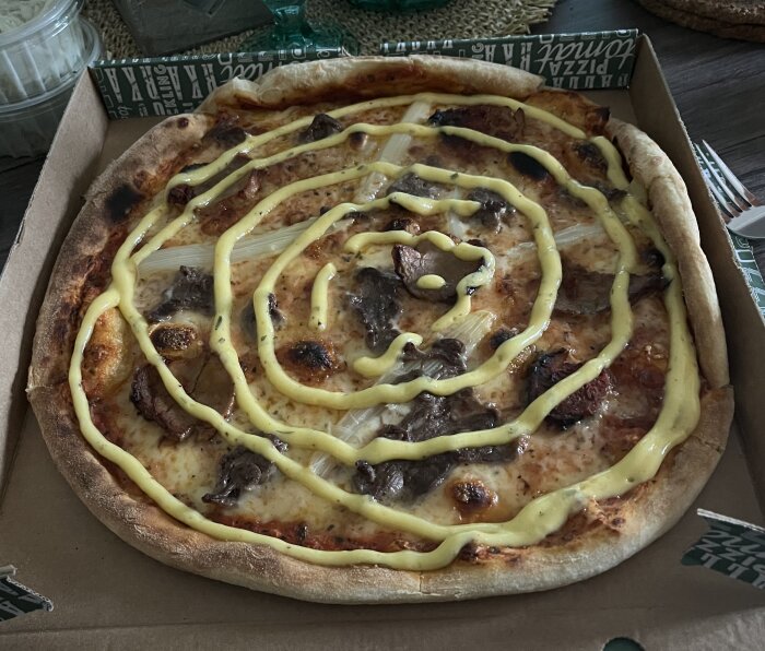 Pizza med oxfilé, fläskfilé, sparris och bearnaisesås i en kartong.