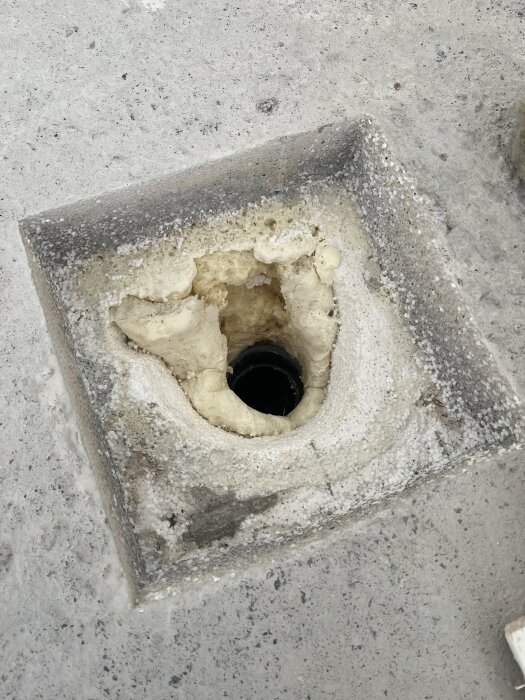 Golvbrunn i tvättstuga efter att frigoliten tagits bort, omgiven av rå yta redo för fallspackling, med synlig hålighet och avlopp.