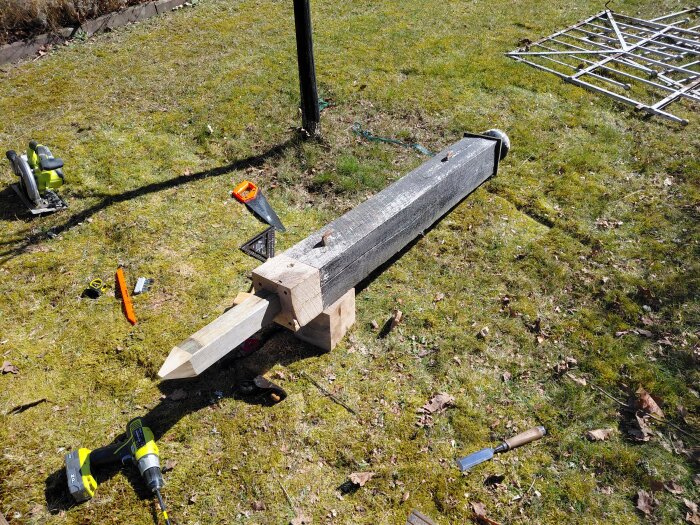 Ruttna delar av en grindstolpe ligger på gräsmatta omgivna av verktyg som såg, borr och vinkelhake vid en nödfix.