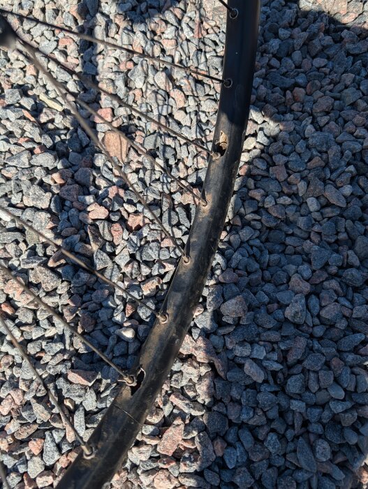 Cykelhjul med flera ekrar och ett hål i fälgen liggande på grått grus.