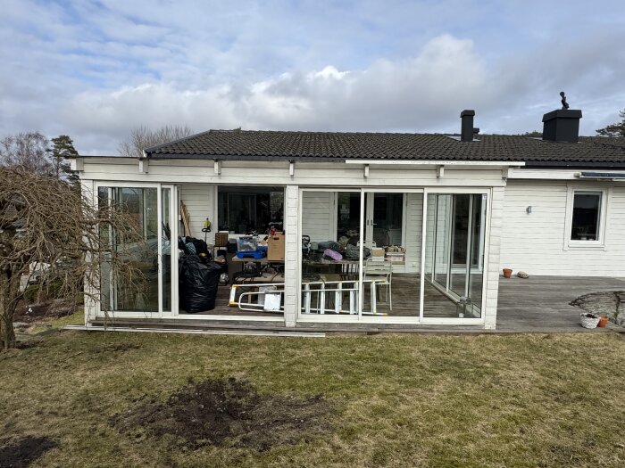 Ett renoverat uterum med vita väggar och stora glaspartier mot en grön trädgård, innehållande byggmaterial och möbler.