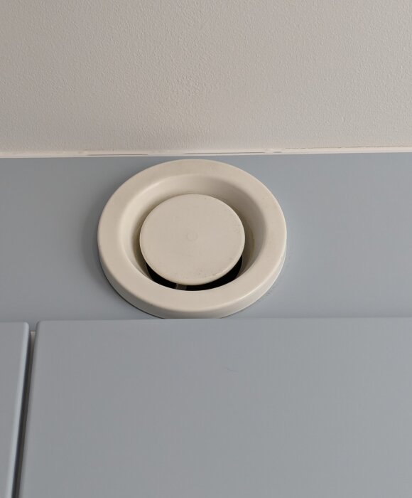 Vit ventilationsventil inbyggd i ett blågrått tak, sedd från sidan.