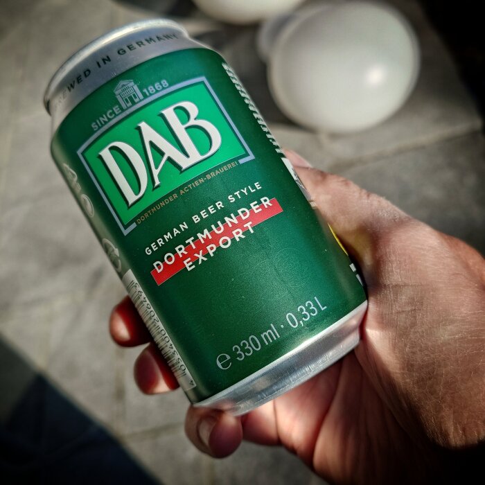 En hand håller en grön burk DAB Dortmunder Export öl, 330 ml.