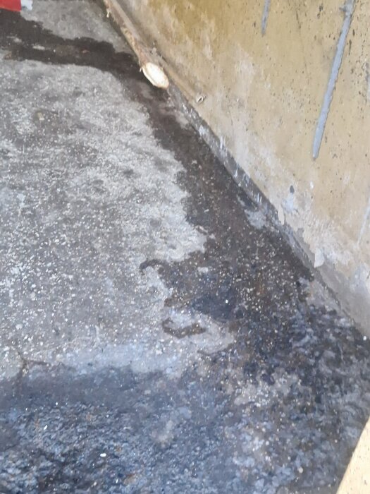 Vattenskada på betonggolv med fuktfläckar längs en vägg.