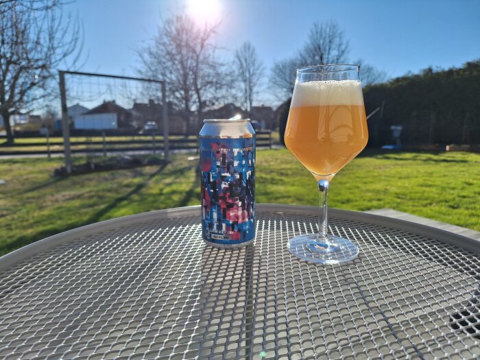 En ölburk och ett glas öl på ett trädgårdsbord i solen, med en grönskande bakgrund.