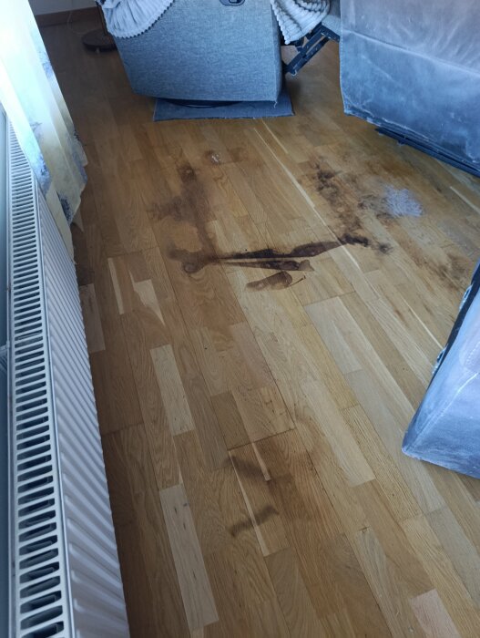 Fläckiga märken på trägolv bredvid en soffa nära ett element.