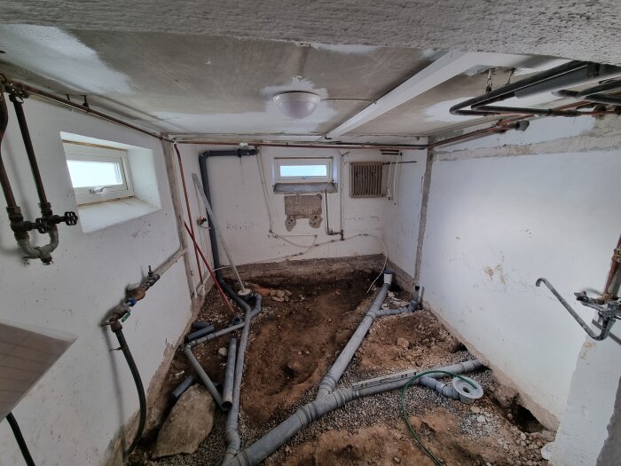 Renoveringsprojekt av källare med uppbrutet betonggolv, synliga avloppsrör och väggar. Rum planerat som badrum under ombyggnation.
