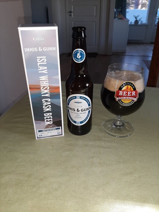 En flaska Innis & Gunn Islay Whisky Cask Beer står bredvid ett glas med öl och en förpackning på ett bord.