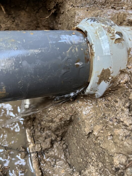 Plast- och metallkoppling i mark med läckage vid skarv i ett bevattningssystem, delvis ingjuten i en pumpbrunn.