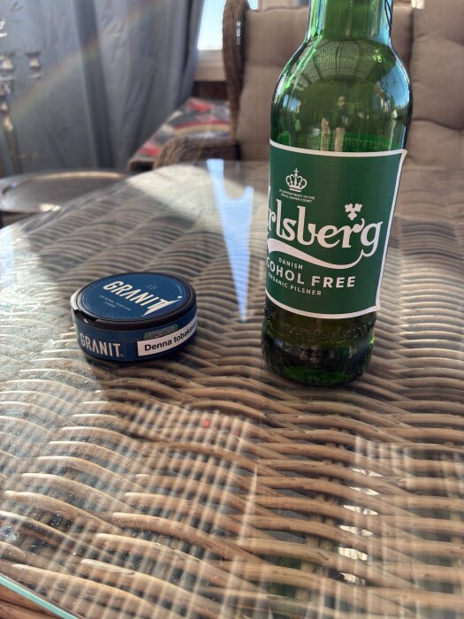 Alkoholfri ölflaska bredvid en snusdosa på ett bord.