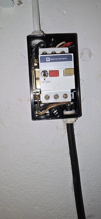 Strömbrytare med märke "Telemecanique" monterad på en vit vägg, med svarta och färgade kablar anslutna.