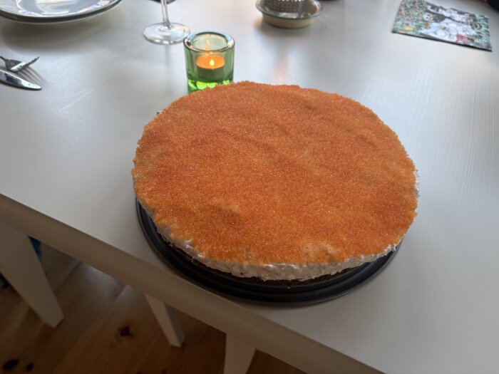 Laxtårta dekorerad med orange kaviar på ett bord, omgiven av en grön ljuslykta och tallrikar.