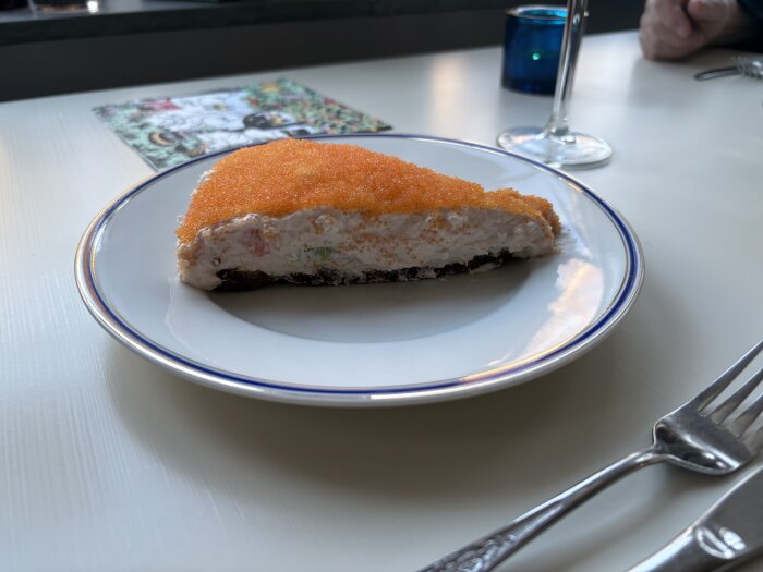 En laxtårta med orange rom topping, serverad på en tallrik, omgiven av bestick och ett glas i bakgrunden.