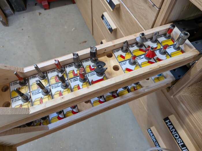 3D-printade hållare för frässtål i utdragbara lådor med etiketter, vid fräsbordet. Plywood med 16mm hål för sortering och märkning.