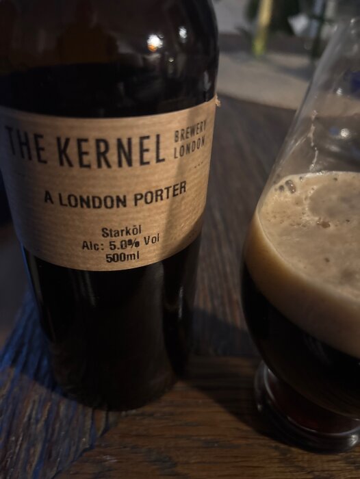 Flaska med London porter från The Kernel Brewery och ett glas med mörk öl på ett träbord.