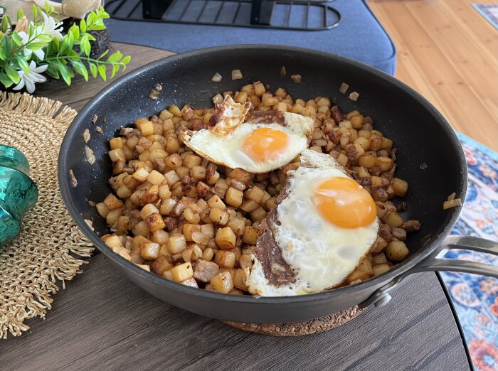 Stekt oxpytt med två stekta ägg i en stekpanna på ett bord med dekorativa föremål.
