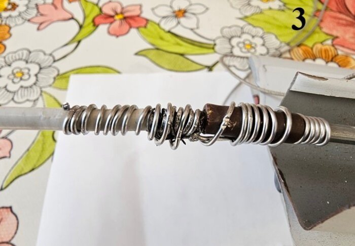 Metallvajer och ståltråd tvinnade runt axel, omgivna av plastpluggar och limmade med Epoxy. Bakgrund med blommönstrad duk och skruvstäd.