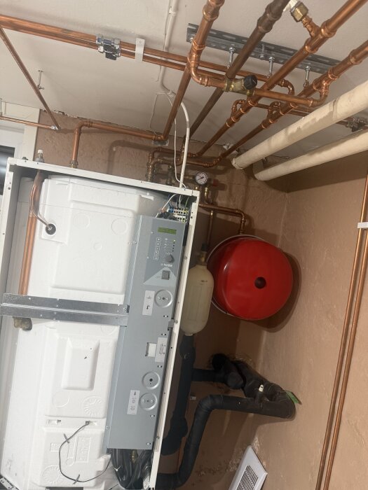 Värmesystem i källare med kopparrör, expansionstank och styrpanel, som kan orsaka återkommande larm.