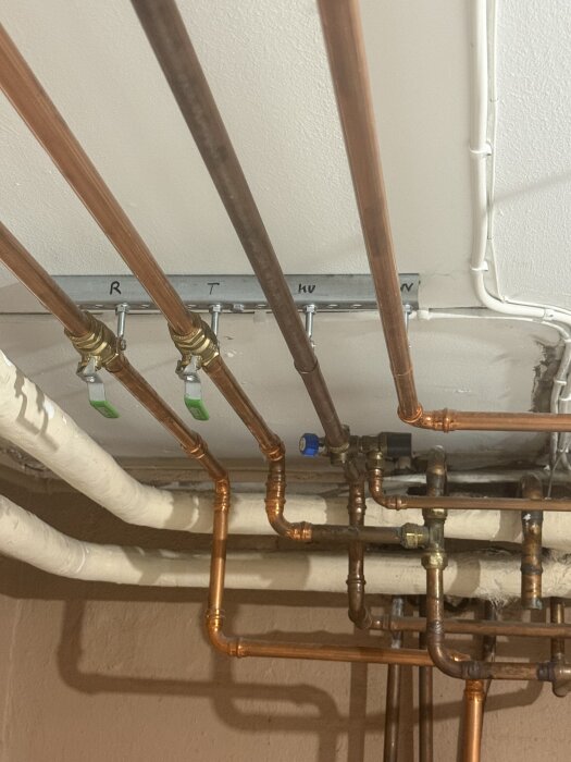 Kopparrör och ventiler i en takinstallation för VVS-system. Flera rör leder i olika riktningar och är kopplade till en central punkt.