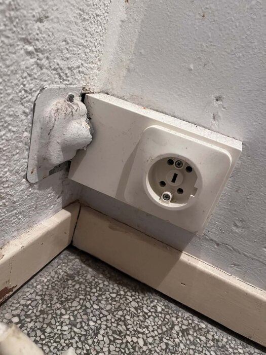 Eluttag vid golv med en oregelbunden installation, synlig kabel och slitet golv i rummet.