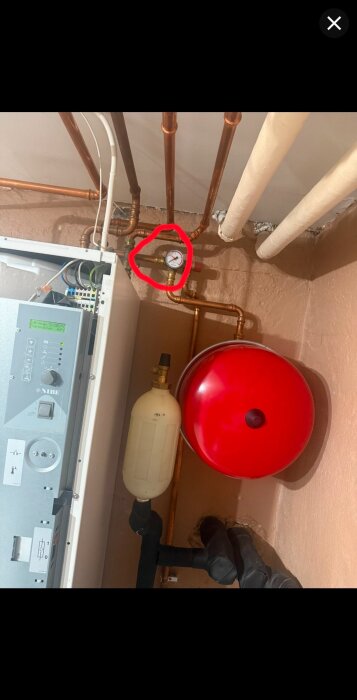 Tryckmätare på ett rörsystem visar noll tryck, omgiven av kopparrör, en vit behållare och en röd trycktank.