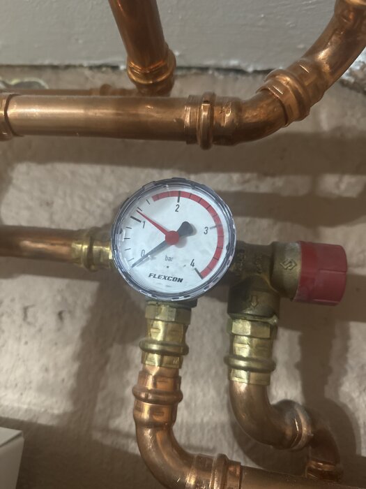 Manometer med röd visare på 1,2 bar, monterad på kopparrör.