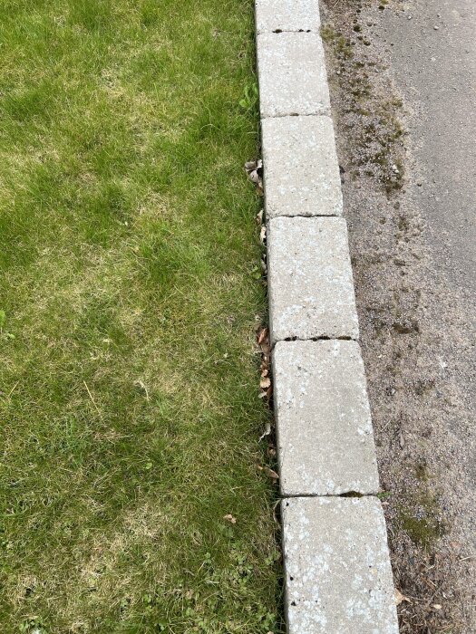 Betongmurar bredvid en gräsmatta och en grusgång, potential plats för staketbygge, sett ovanifrån.