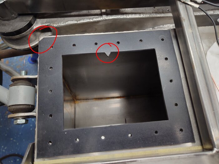 Del av metallstruktur för grenrör, där hål och svetsfogar syns, markerad med röda cirklar för detaljvisning.