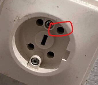 Närbild av ett eluttag i vägg med en röd markeringsring runt en skruv.