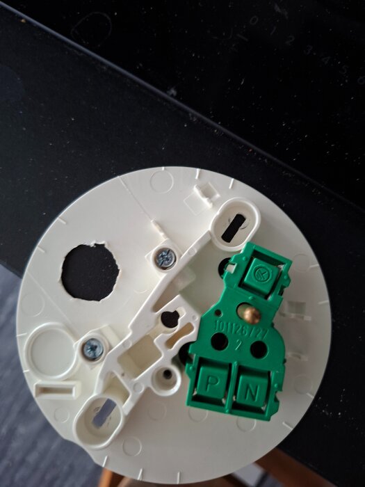 Vit plastplatta med gröna elektriska anslutningar, monterad med skruvar.