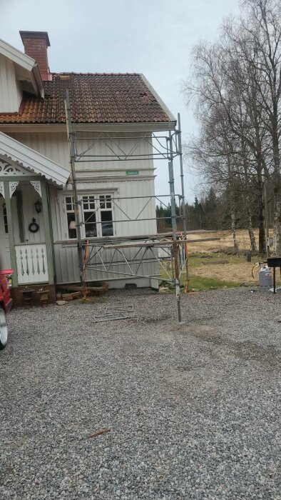 Byggställning vid husfasad med takpannor och träd i bakgrunden. Ställningen används för reparation av taket.