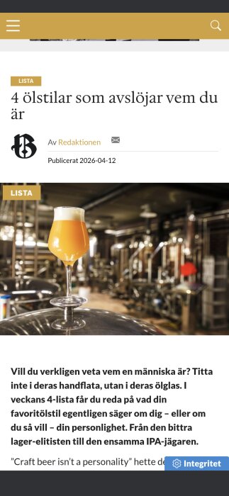 Ett glas apelsinfärgad öl står på en ölbehållare i ett bryggeri, med suddiga bryggerirör i bakgrunden.